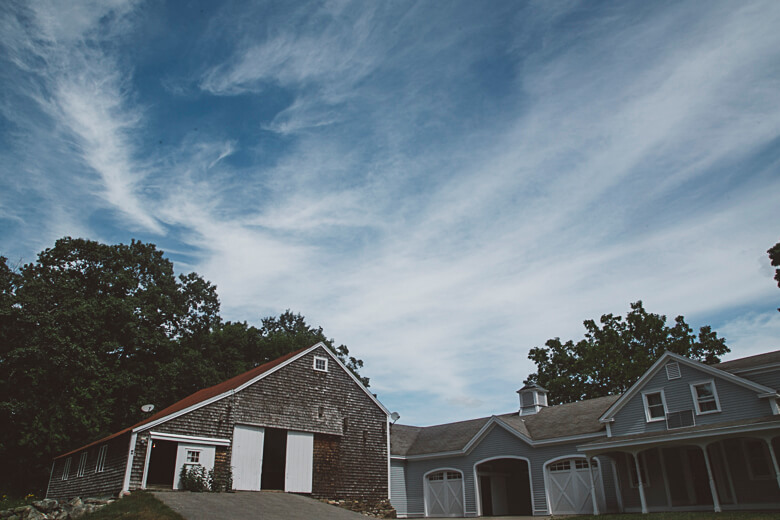 Rustic shingle-sided barn and gray house under wispy blue sky