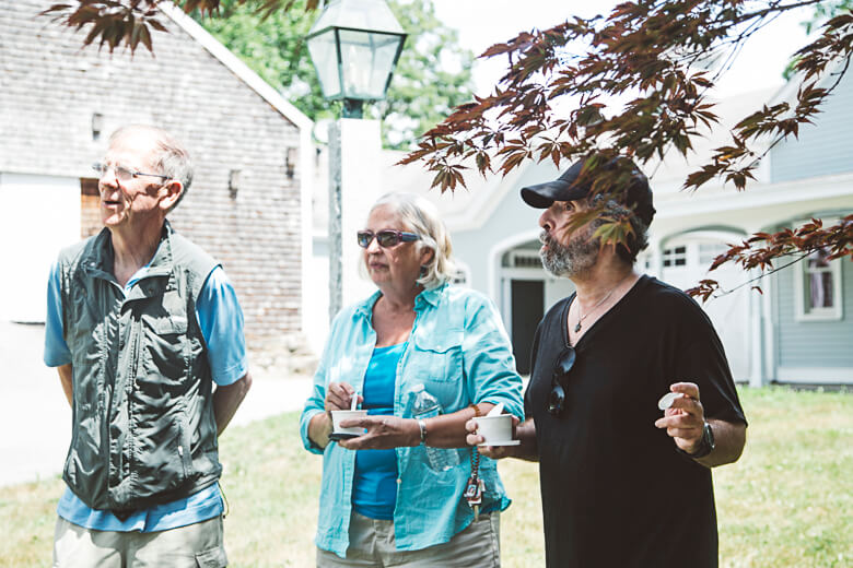 Three older adults standing outside, drinking coffee near a lamppost