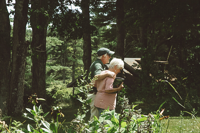 Elderly couple walking together in a lush, green forest with flowering plants