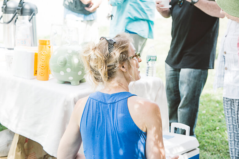 Woman in blue tank top at outdoor event with water bottles and containers