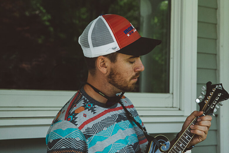 Musician in colorful shirt and trucker cap playing mandolin by window