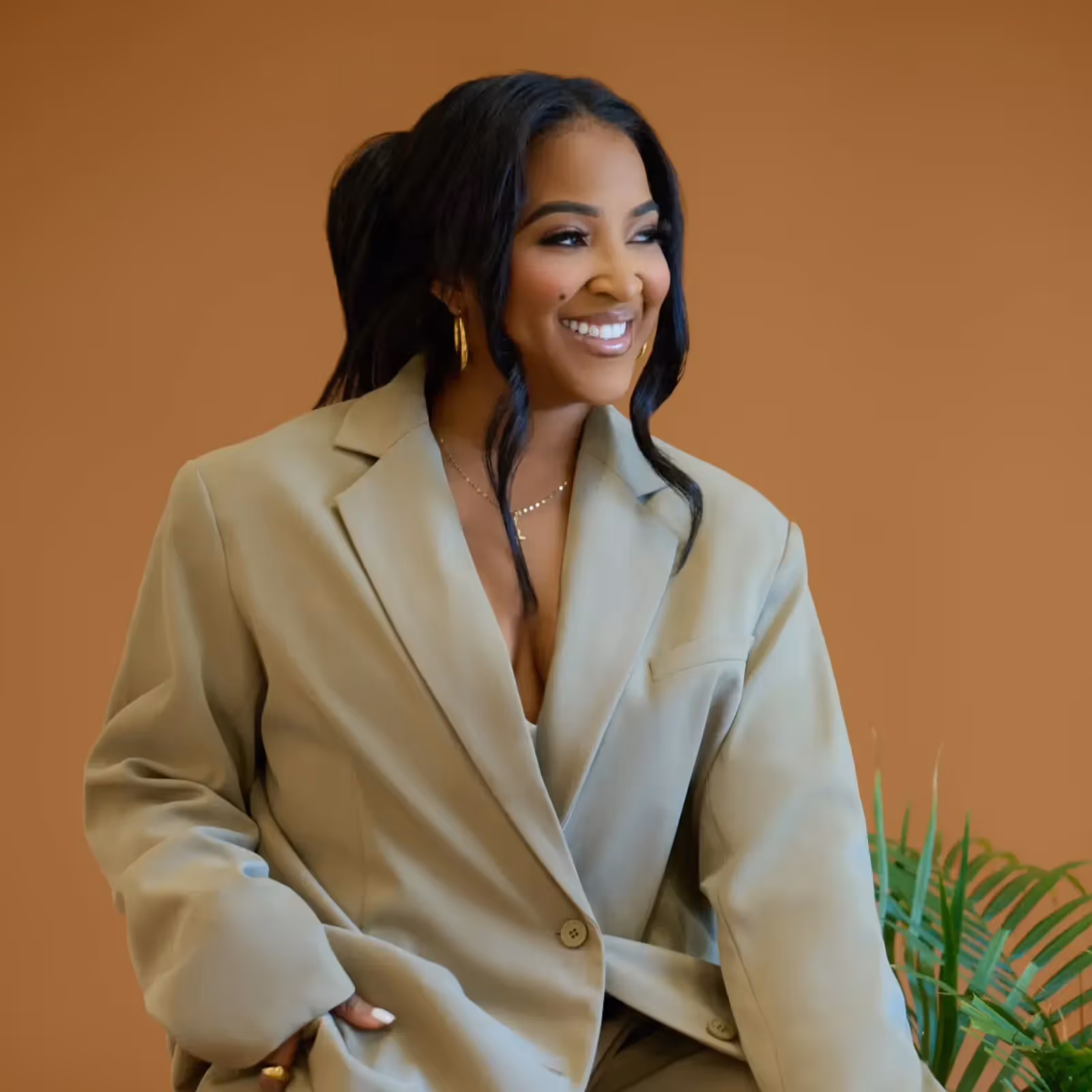 Smiling woman in an oversized beige blazer looking to the side.