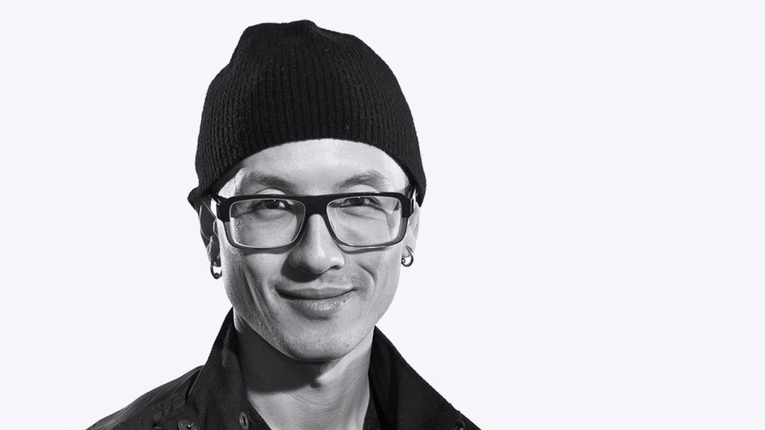 Black and white portrait of a smiling man wearing a knit beanie and glasses.