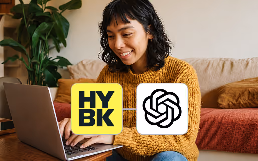 A woman in a mustard yellow sweater smiles while typing on a laptop, with two logos superimposed: the yellow and black HYBK logo and the black and white OpenAI logo.