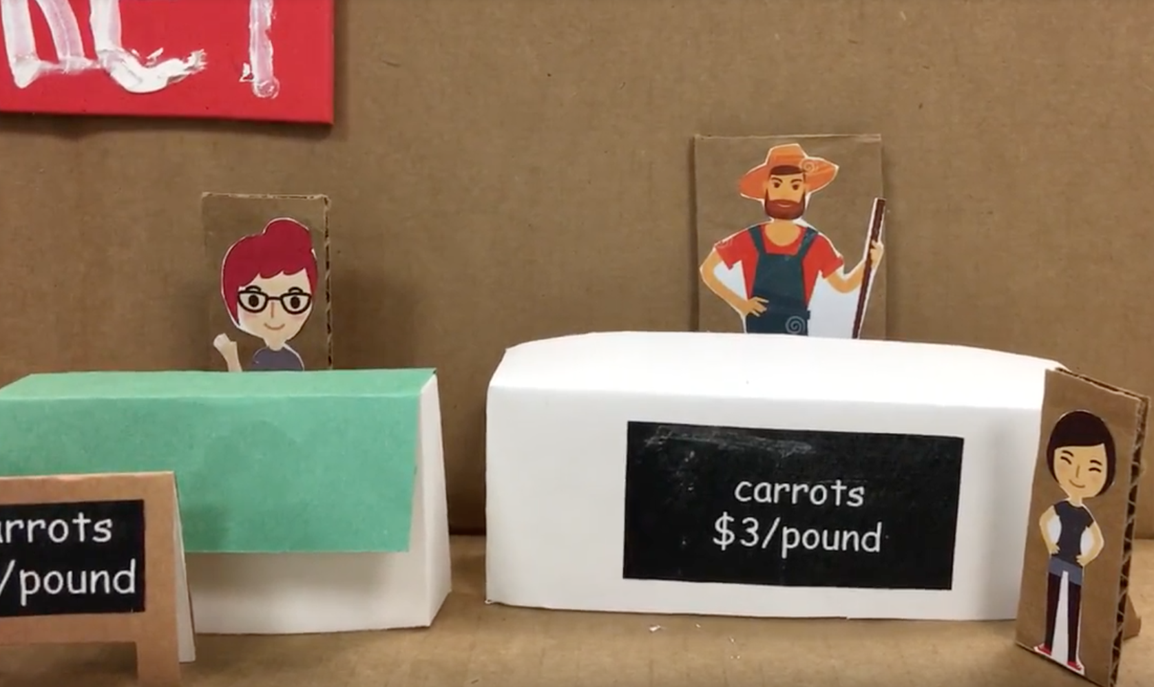 Low-fidelity paper prototype of a farmers market carrot stand with cardboard cutout characters and a pricing sign