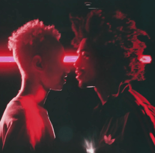 Animated glitch art of two people face to face in red light, with a streak of pink light flickering behind them