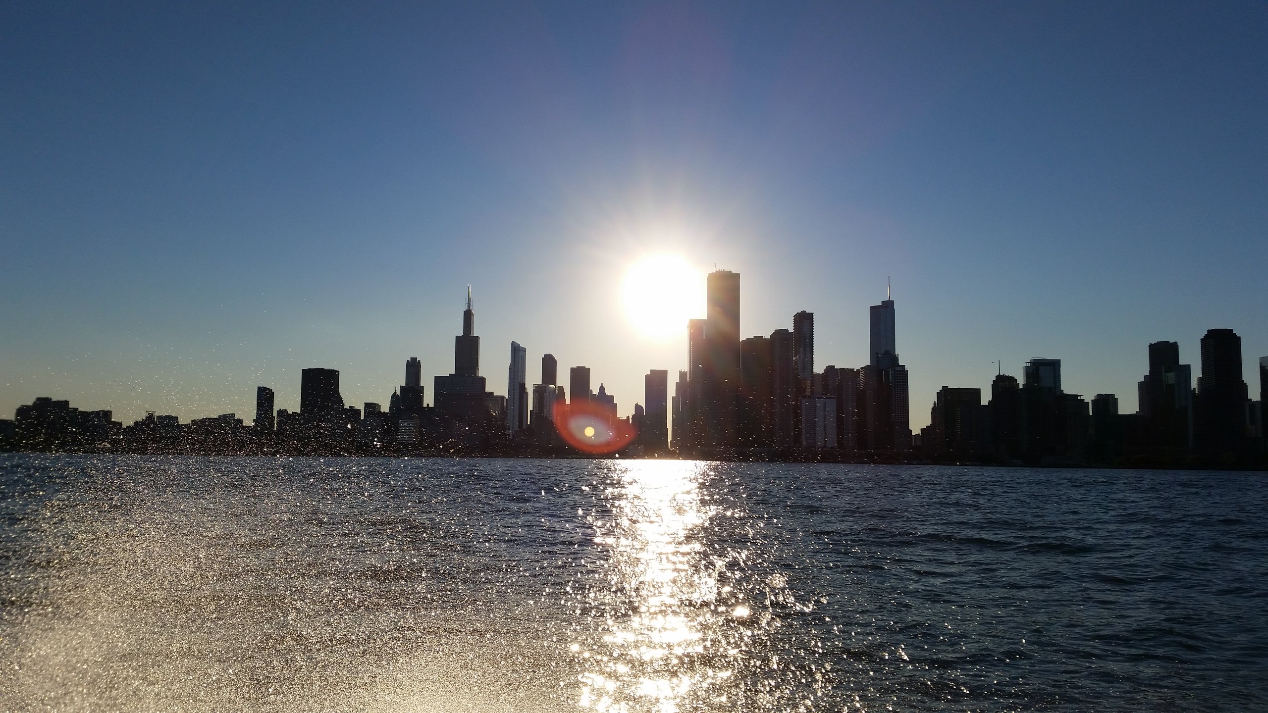 Chicago skyline in silhouette at sunset, seen from Lake Michigan with sunlight glittering across the water