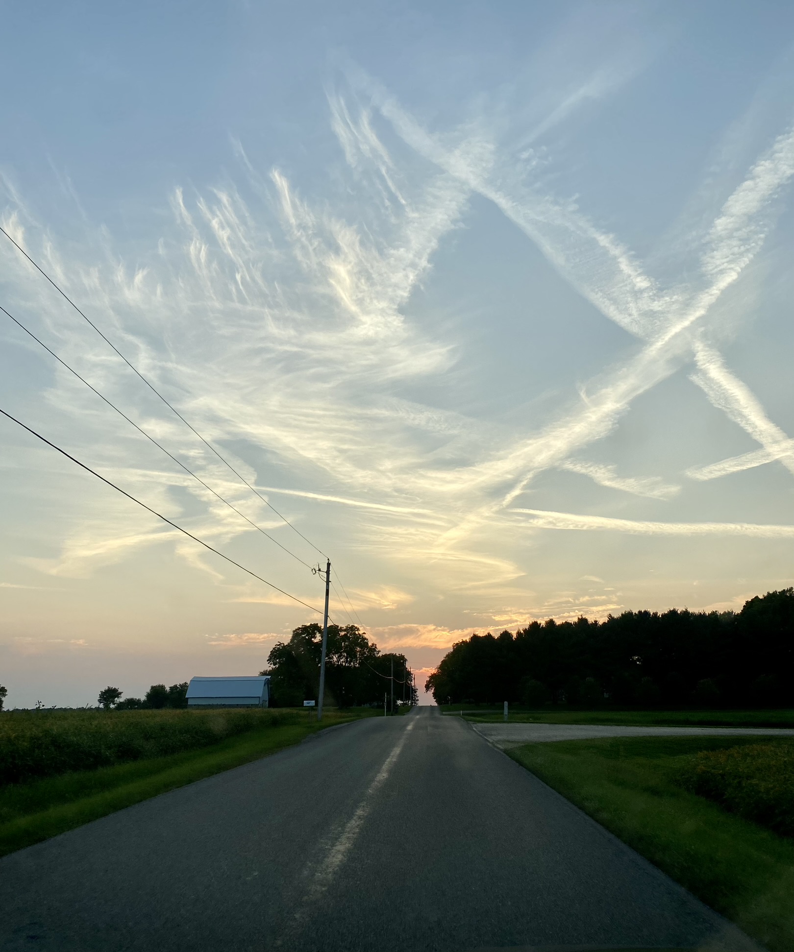 Empty country road at sunset under a sky crisscrossed with wispy clouds and contrails