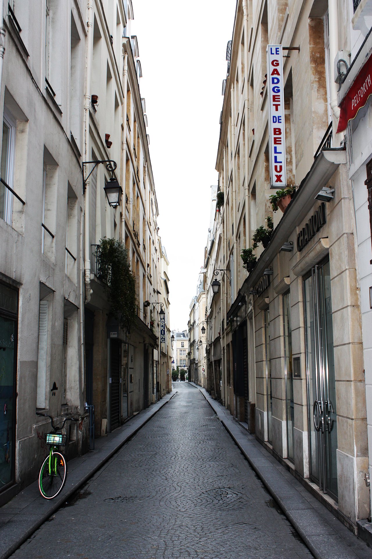 Narrow, empty cobblestone street lined with tall cream-colored buildings, with a green bicycle parked on the left