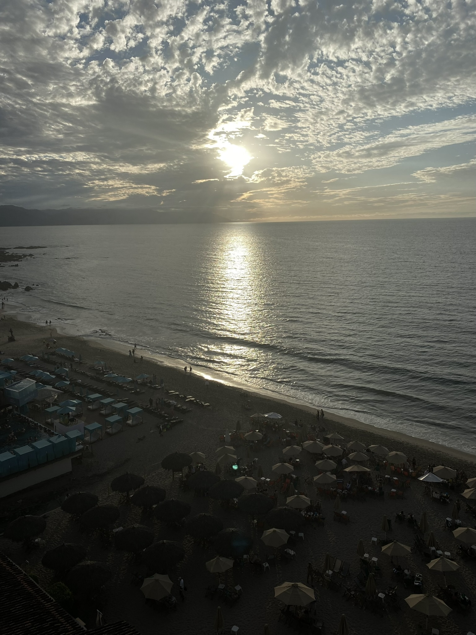 View from above of a beach lined with umbrellas at sunset, with the sun reflecting across the ocean