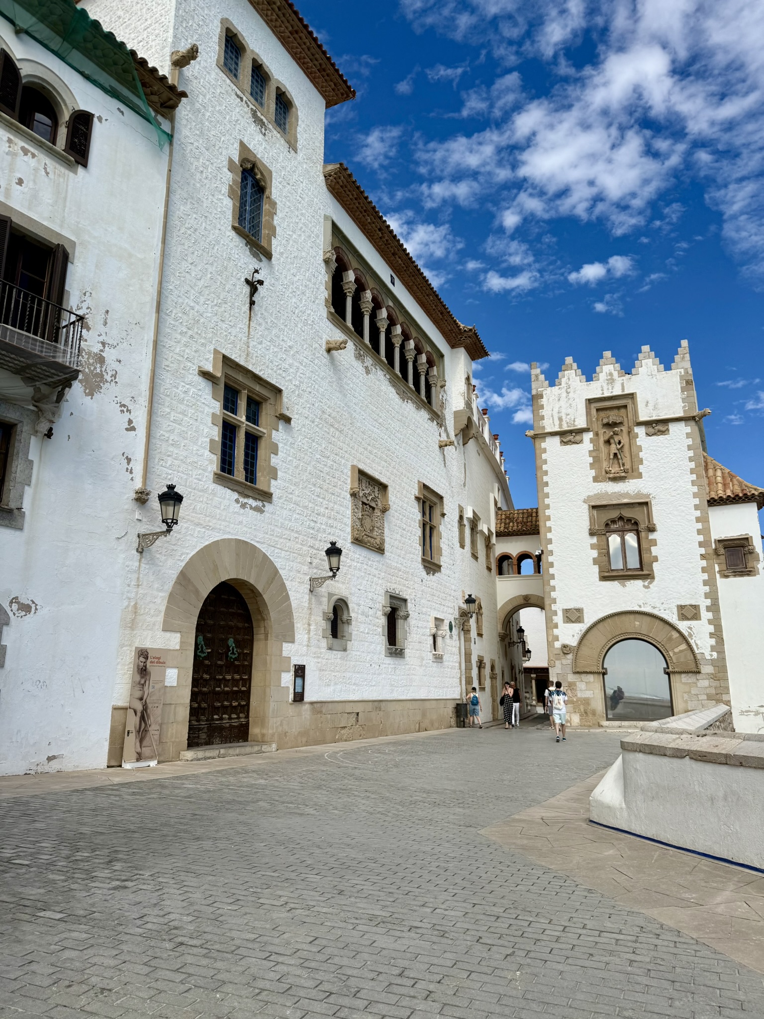 Whitewashed stone buildings with arched doorways and ornate windows around a sunny cobblestone plaza