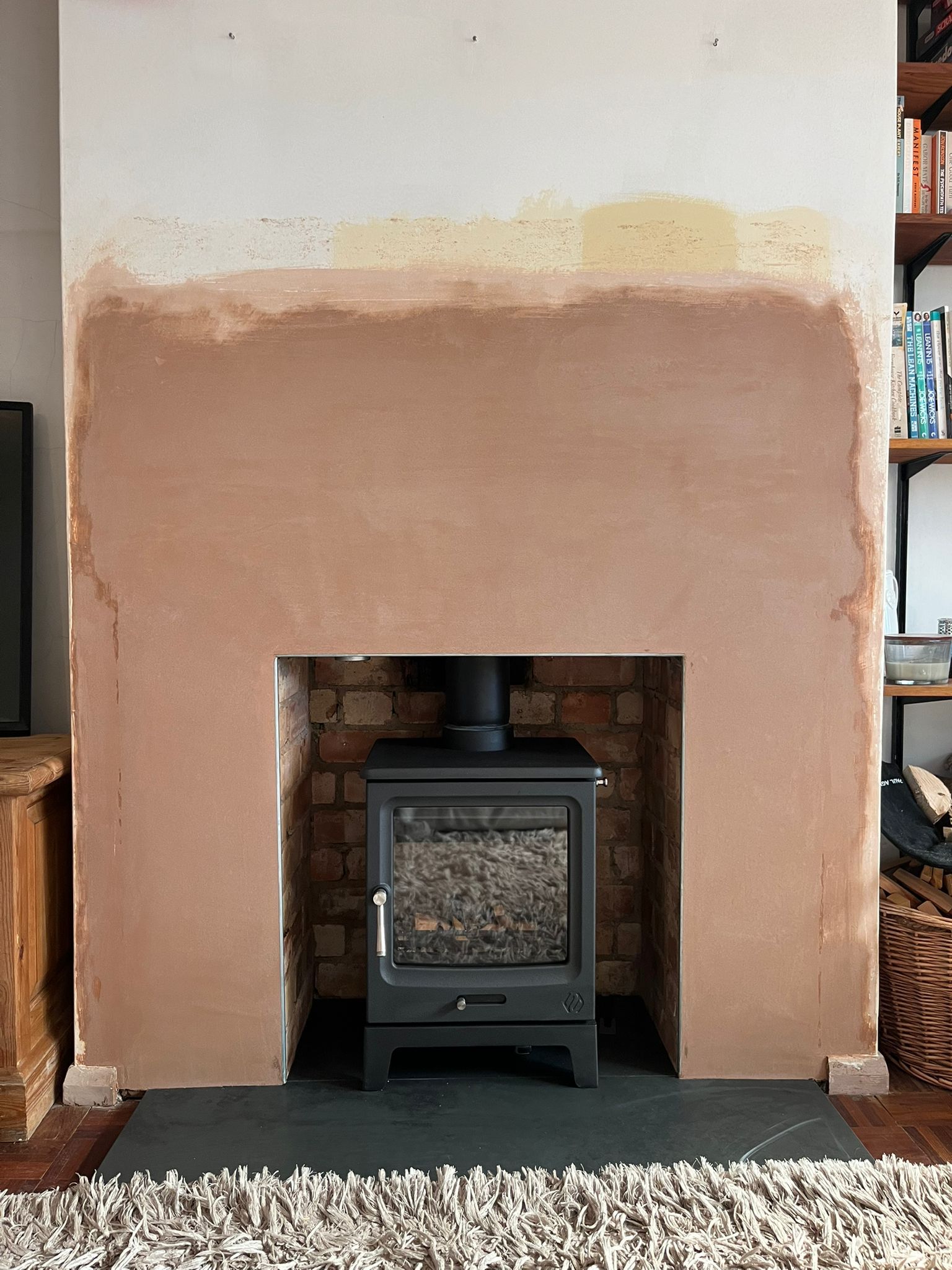 Black wood-burning stove set in a brick fireplace with partially plastered surrounding wall and a shaggy beige rug in front.