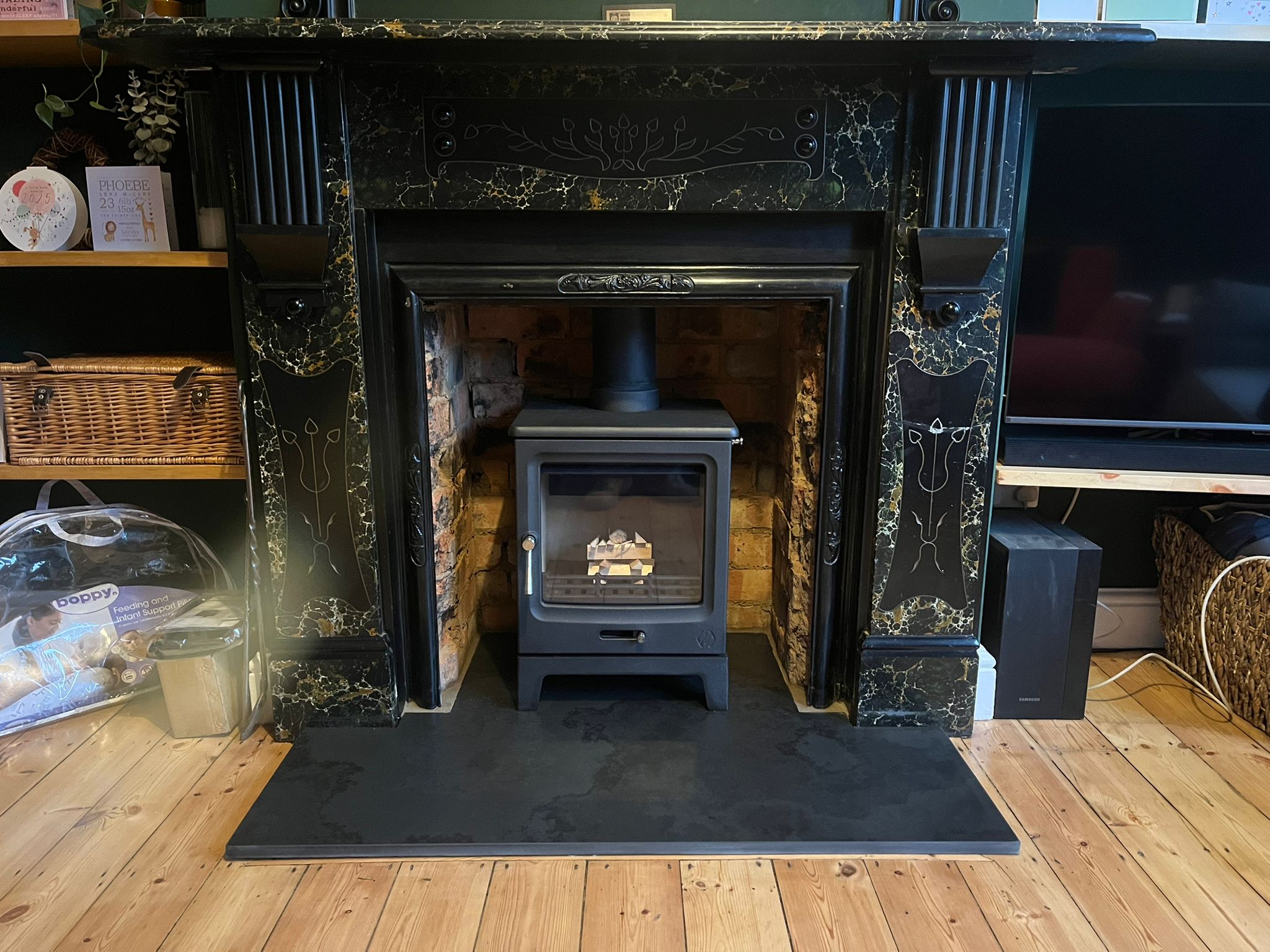 Black wood-burning stove inside a black marble fireplace surround with exposed brick interior on a wooden floor.