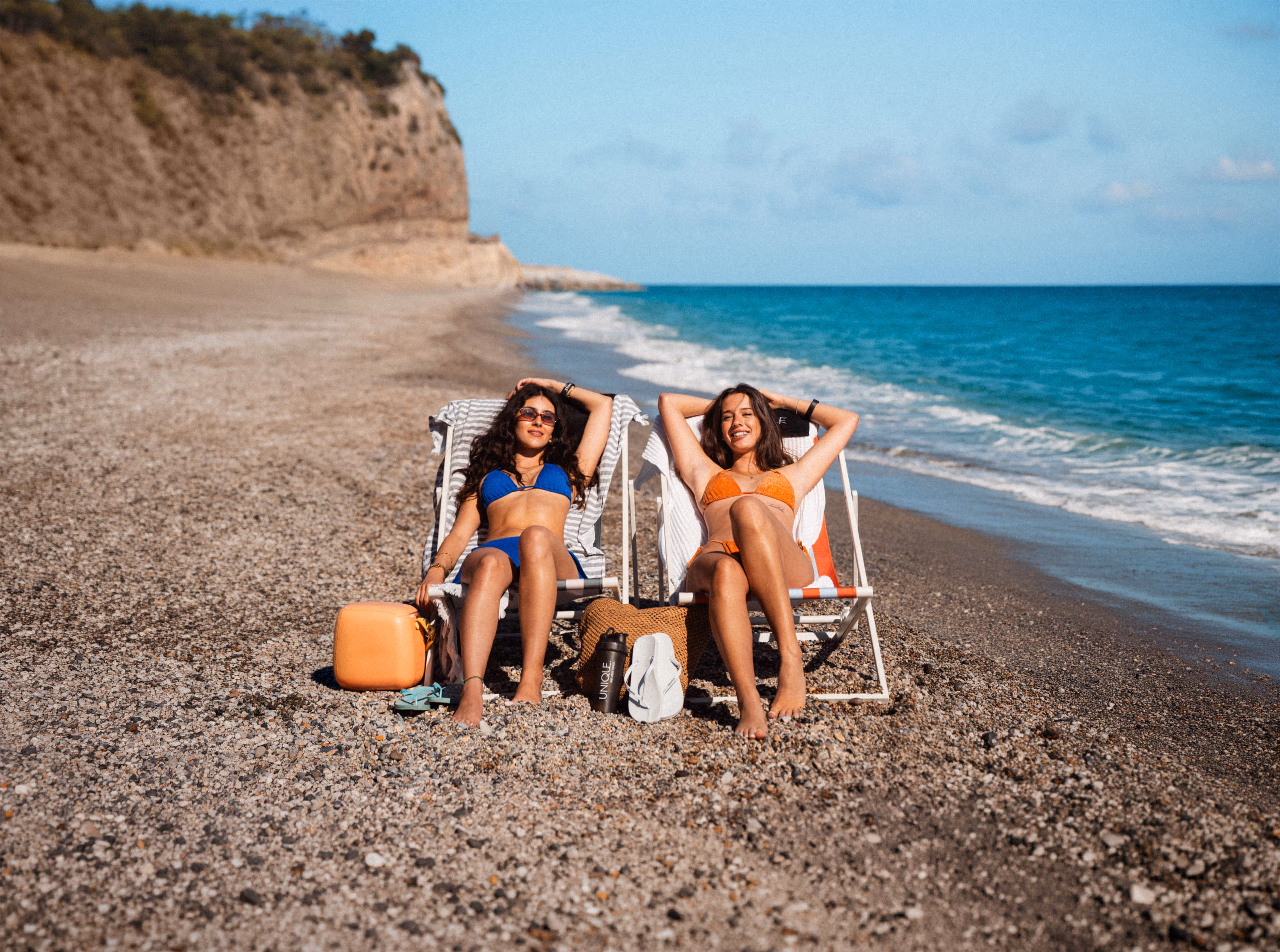 Frühlingskampagne 2026 von UNIQUE Fitness: Zwei Frauen entspannen am Strand mit Sommer- und Ferien-Vibes – Visual für Aktion mit Abo-Rabatt und Gewinnspiel (Reise für 2).