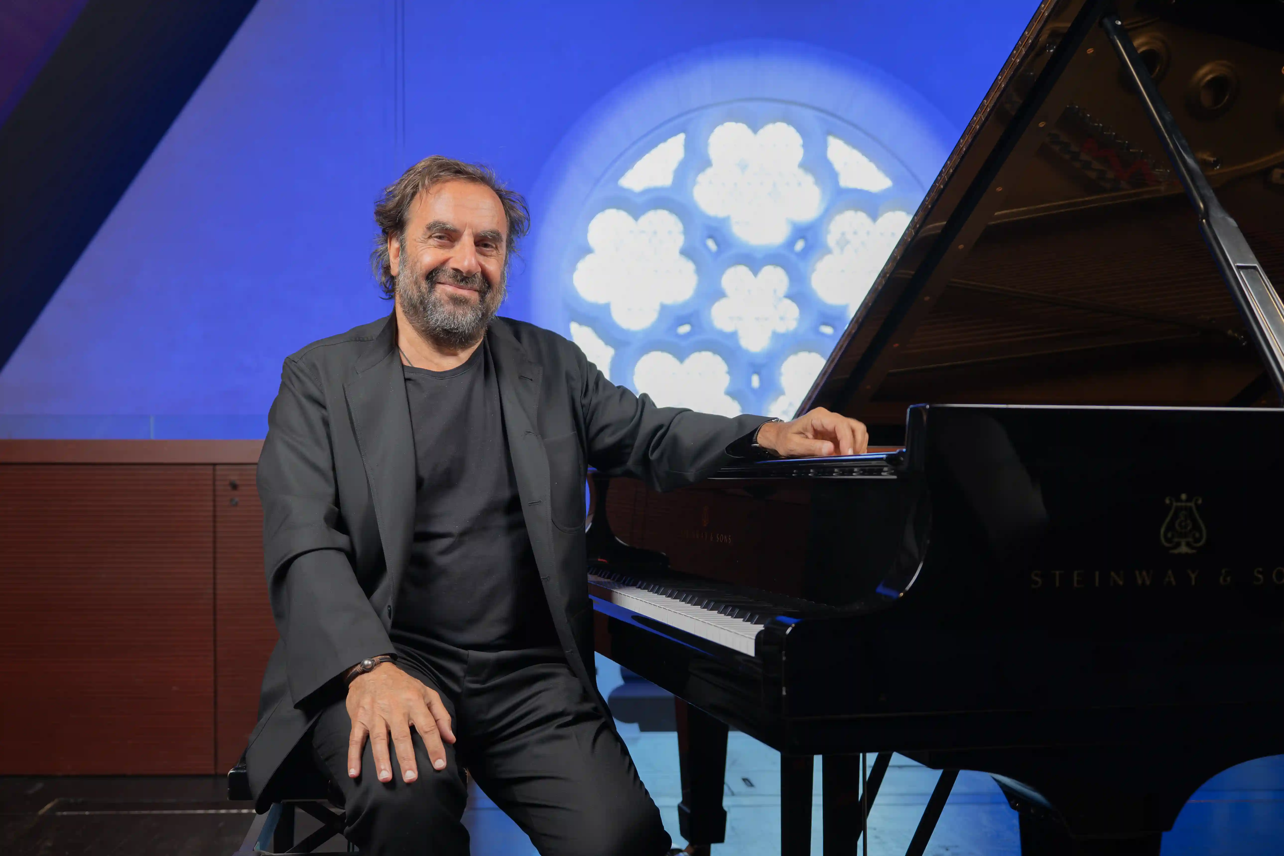 André Manoukian souriant, assis au piano devant la rosace projetée