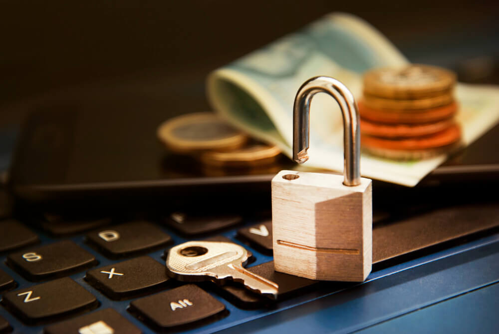 Unlocked padlock and key on a laptop keyboard with coins and a folded banknote in the background.