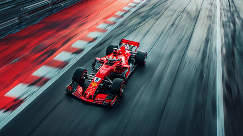 Red Formula 1 race car speeding on a racetrack with blurred asphalt and red and white curbs.