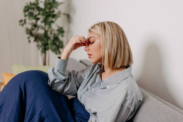 Woman on couch pinching bridge of nose feeling drained from insulin resistance signs.