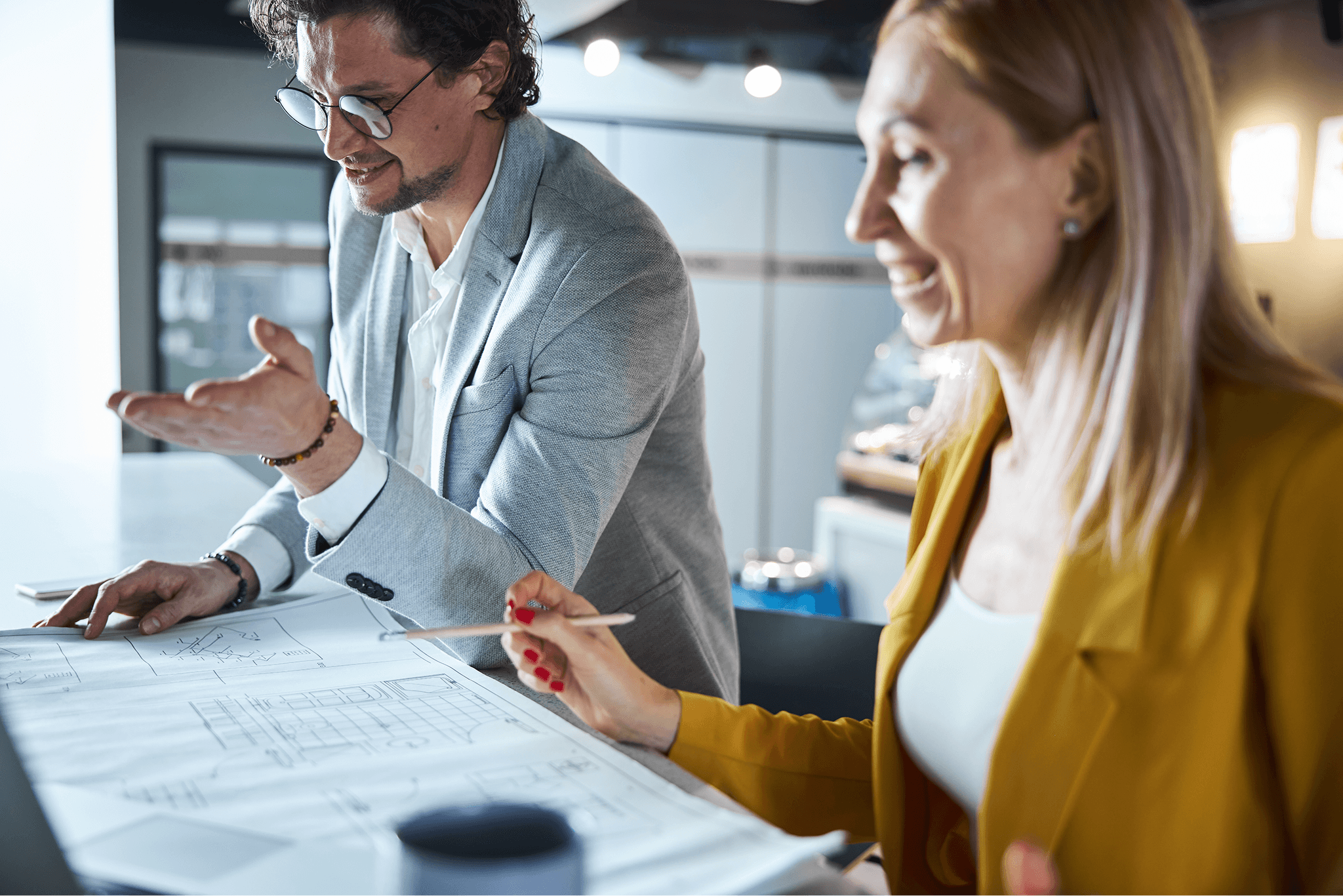 Man and woman discussing architectural blueprints at a table in an office setting.