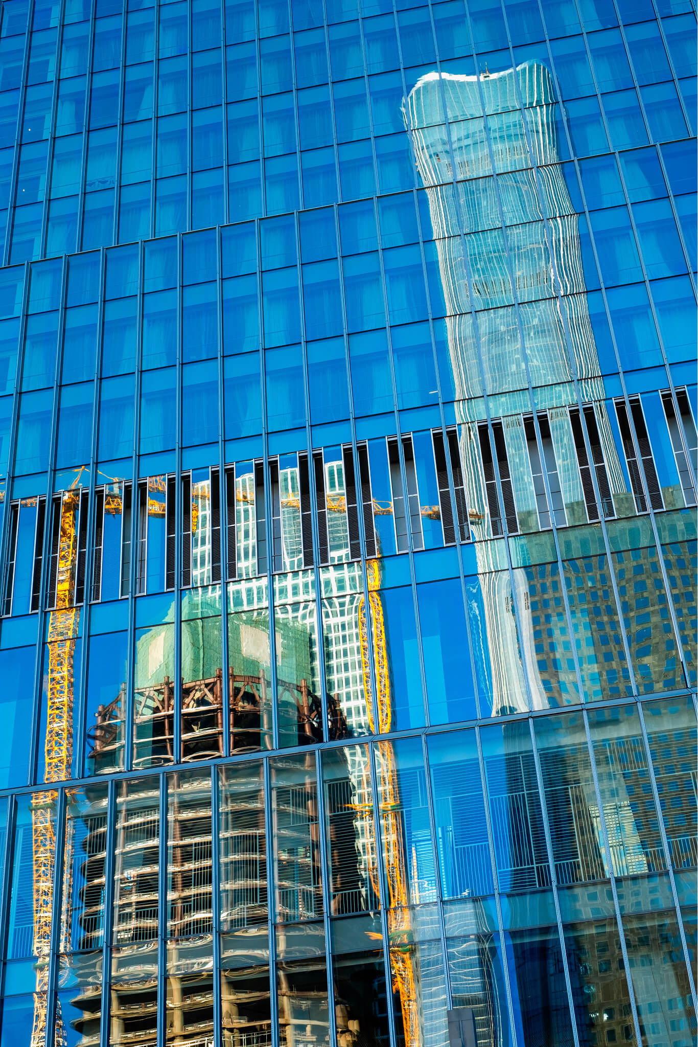 Reflection of construction site and skyscrapers seen on a modern blue glass building facade.