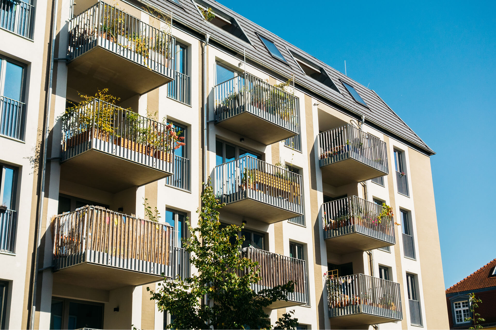 Modern apartment building with balconies featuring plants and railings under a clear blue sky.