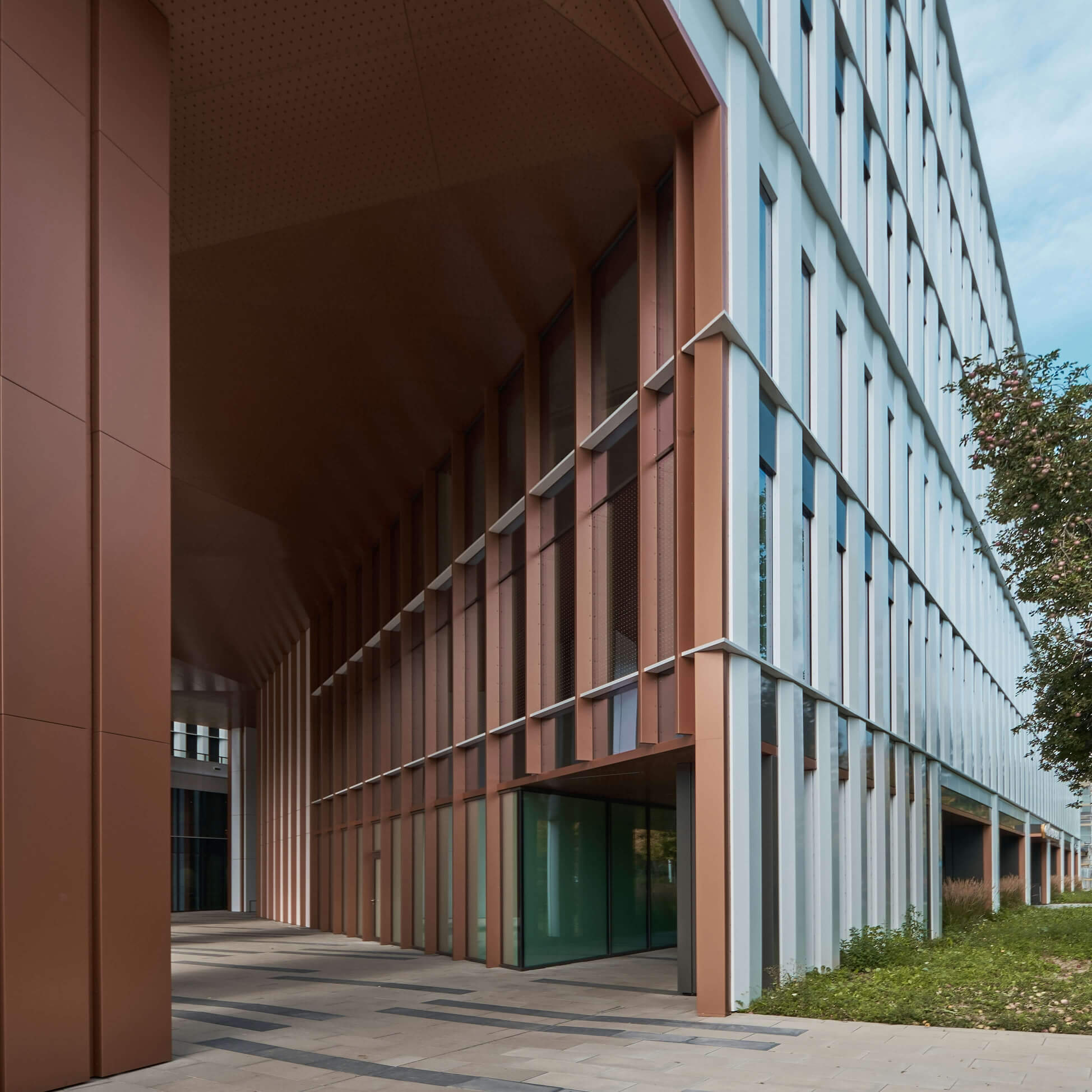 Modern building facade with vertical bronze and white panels and glass entrance under a covered walkway.