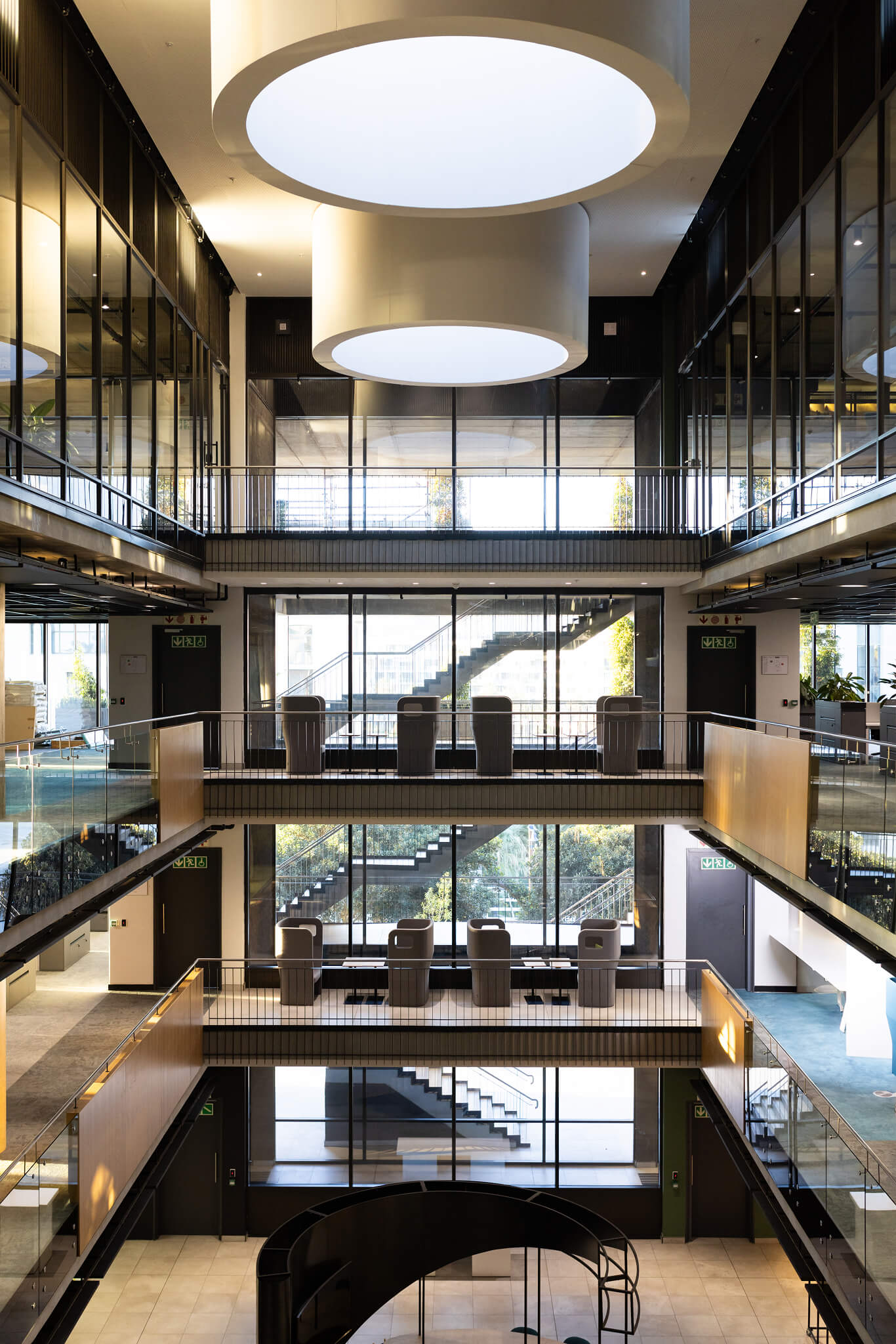 Modern multi-story office atrium with large circular ceiling lights and glass partitions.
