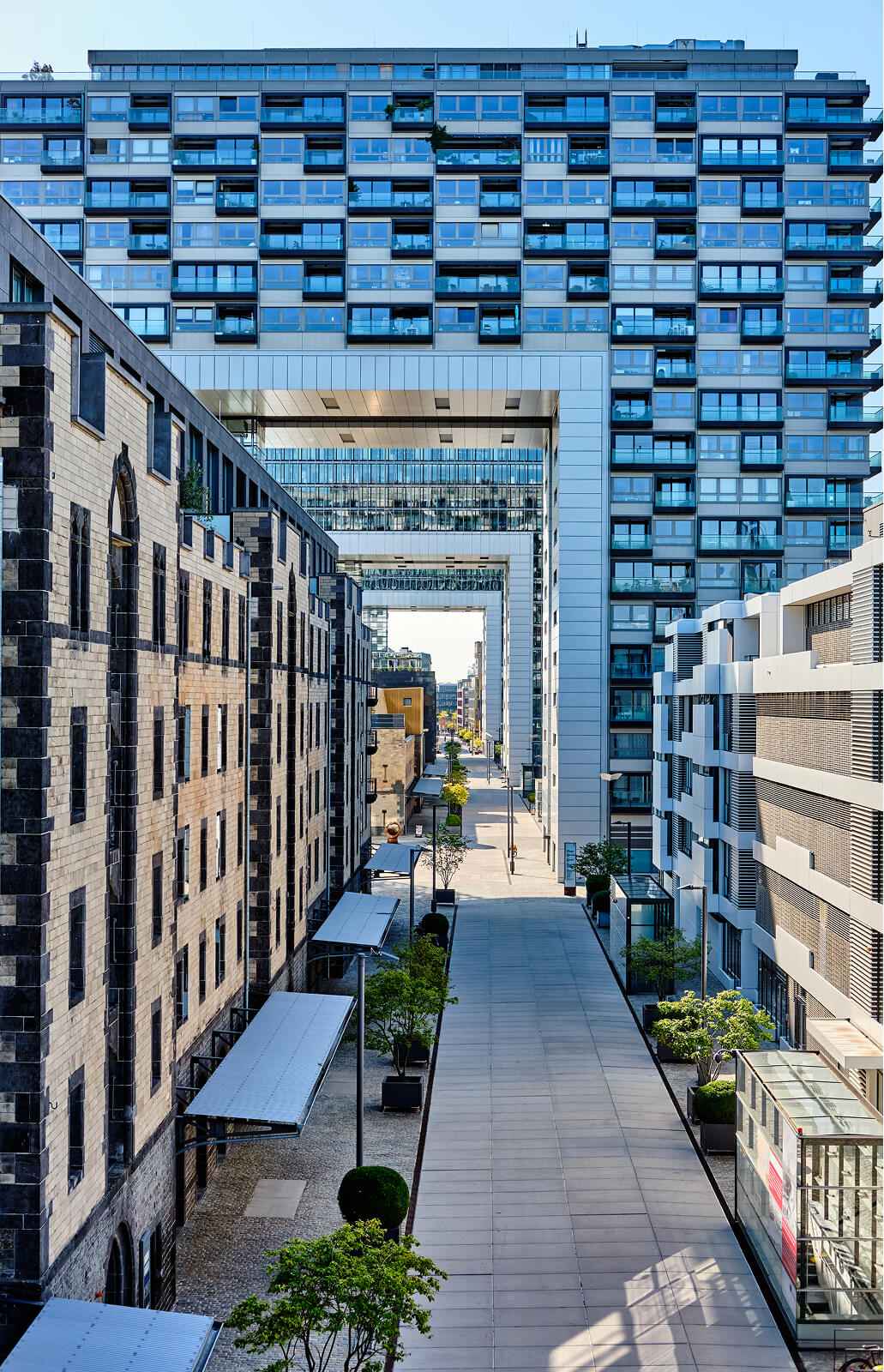 Modern urban street lined with buildings and large rectangular building arches overhead.