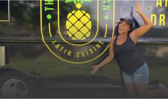 A happy business loan recipient stands joyfully in front of her food truck.
