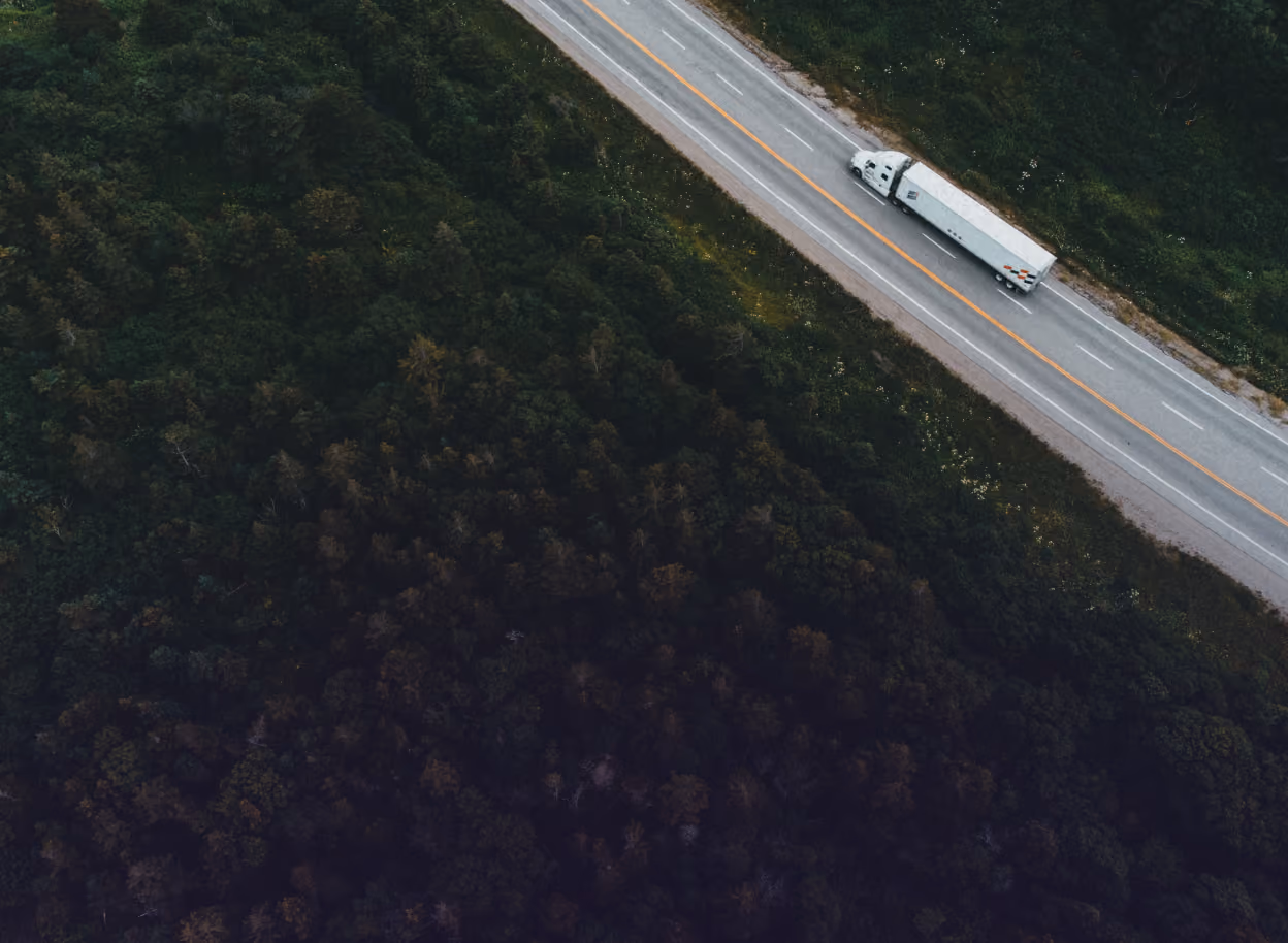 Drohnenaufnahme eines Container-Lkw, der tagsüber auf einer von Wald gesäumten Autobahn fährt
