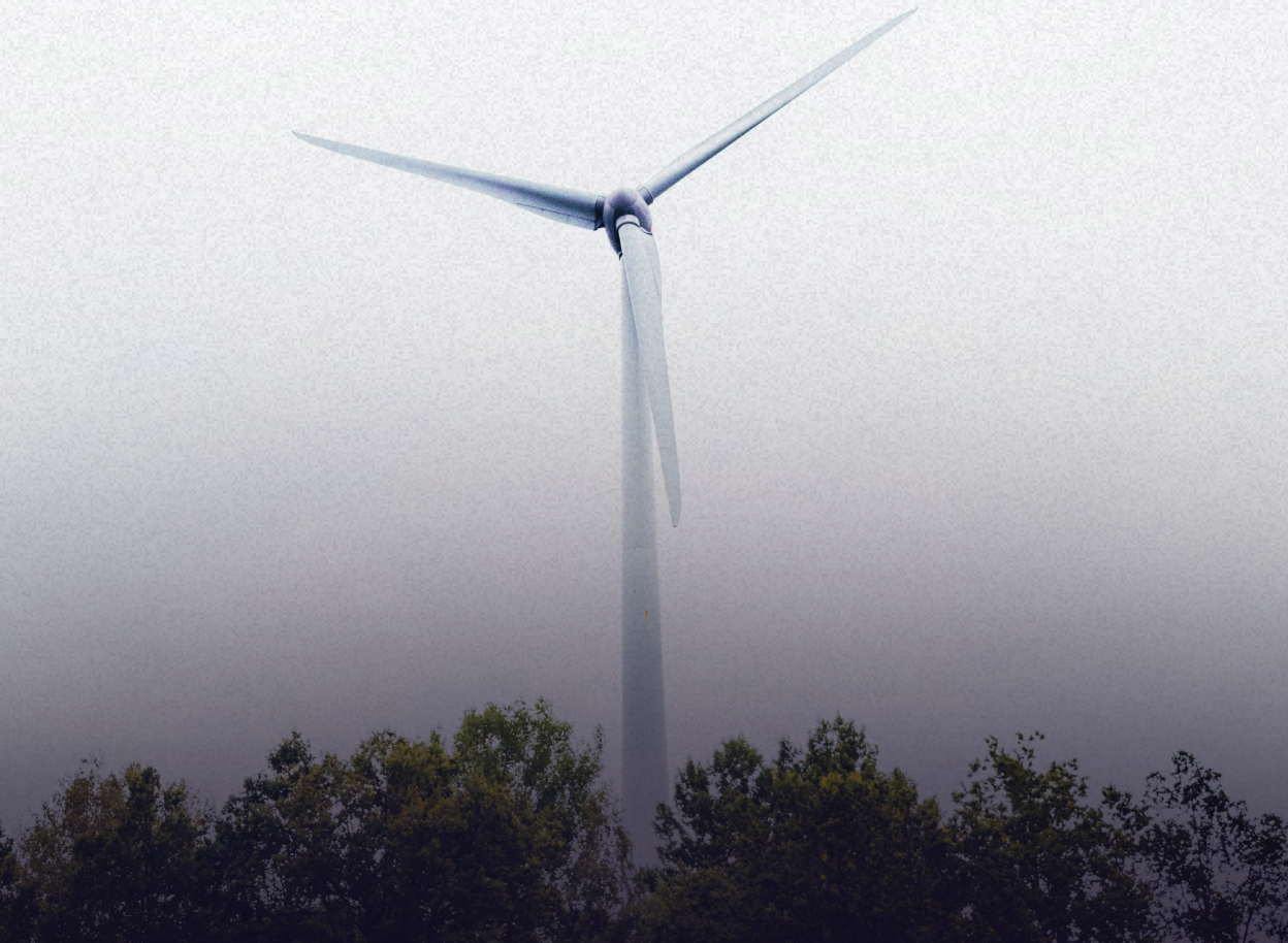 Wind turbine above a forest in foggy weather, symbolizing renewable energy.
