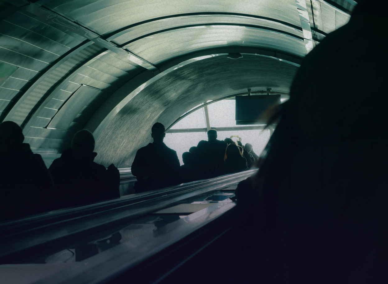 Eine stimmungsvolle Szene auf einer Rolltreppe mit Silhouetten in einer unterirdischen städtischen Kulisse.