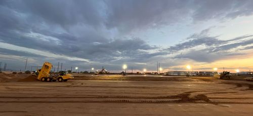 A road illuminated by streetlights, with buildings visible in the background under a partly cloudy sky.