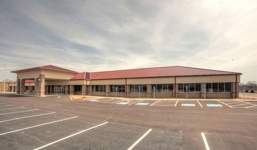 A modern single-story building with a red roof, a covered entrance, and a large empty parking lot.