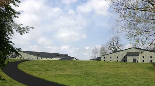 A collection of buildings situated on a hill, surrounded by grass and trees under a cloudy sky.