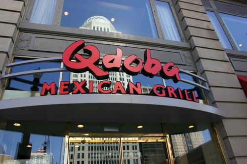 A restaurant sign reading "Qdoba A MEXICAN GRILL" displayed on the exterior of a building,
