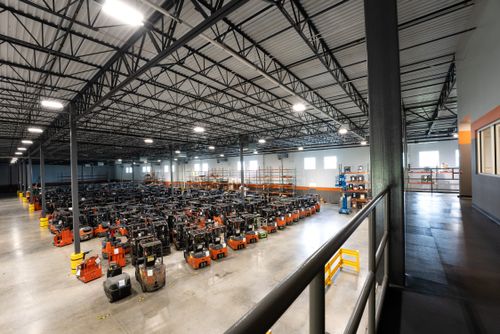 A spacious warehouse filled with various machines, featuring a high ceiling and organized parking areas for the equipment.