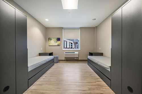 A room featuring two beds, with an interior design that includes walls, flooring, and a plaster ceiling.
