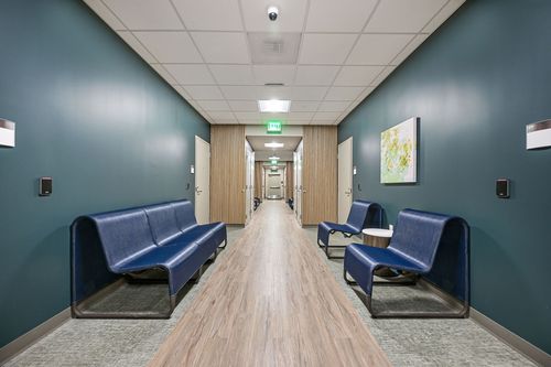 A long hallway featuring blue chairs lined along the sides, with a wooden floor beneath.