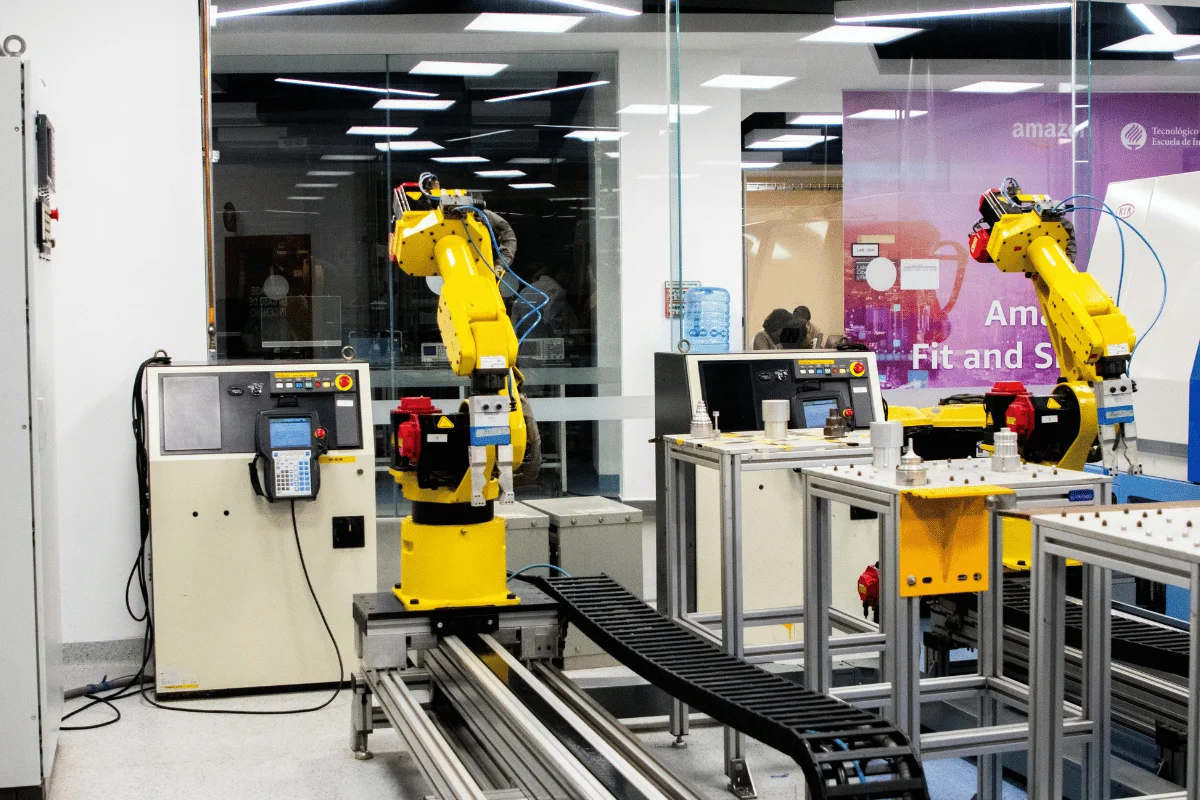 Two yellow robotic arms in a modern industrial lab, positioned on tracks with control panels and workstations nearby.