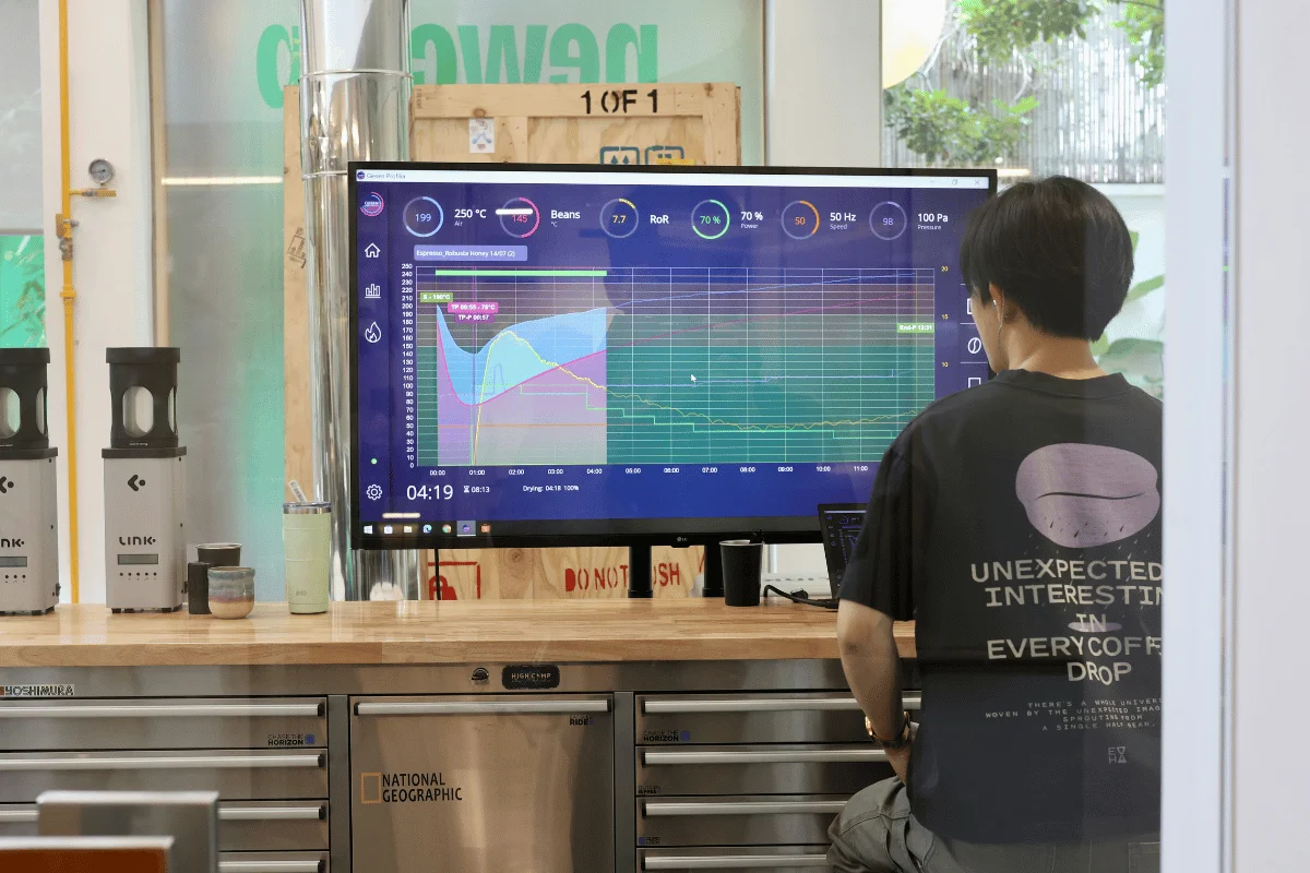A person in a dark shirt monitors graphs on a large screen showing temperature and stats.