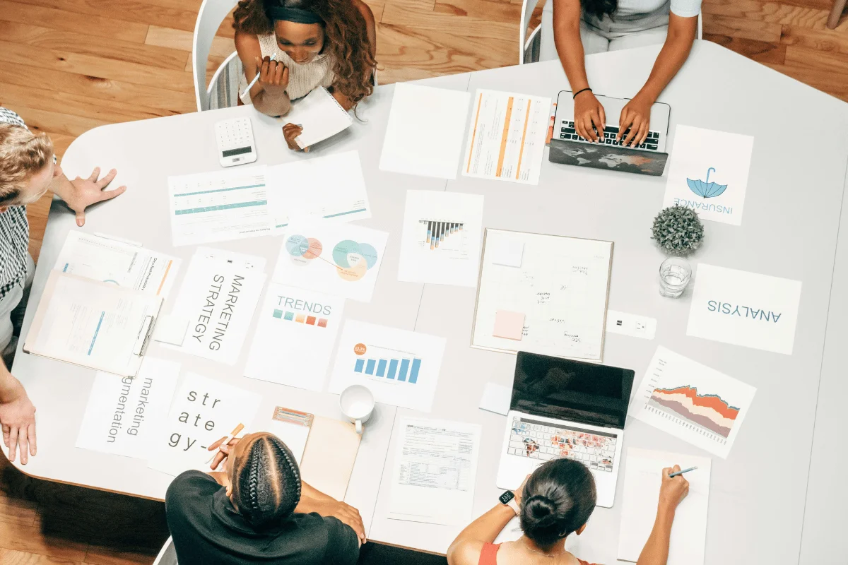 Overhead view of a team meeting with marketing strategy papers, charts, and laptops on a table.