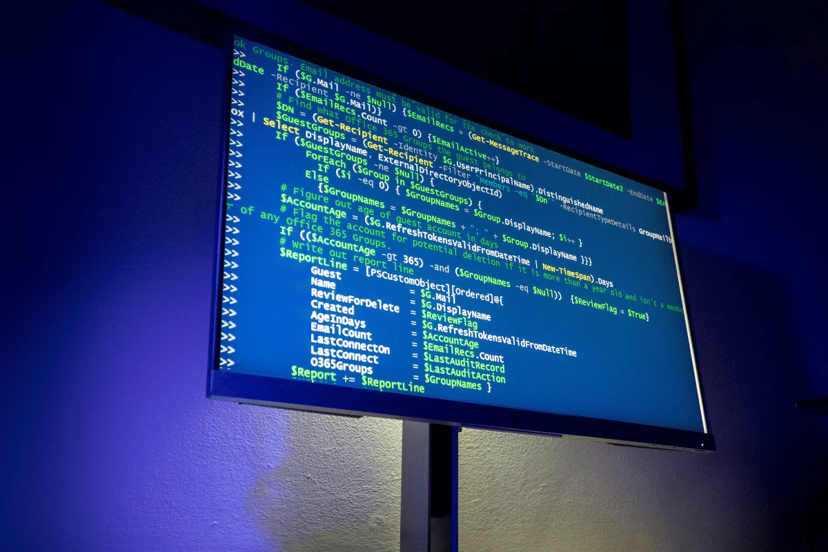 Large monitor displaying code or script output in a dark room with blue ambient lighting.