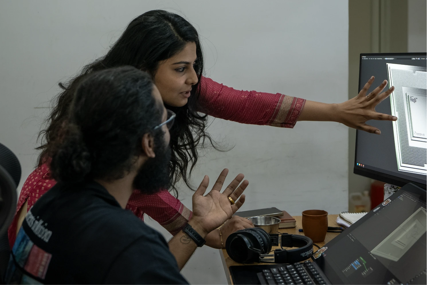 Two people discussing and pointing at a computer screen displaying a layered diagram in an office setting.
