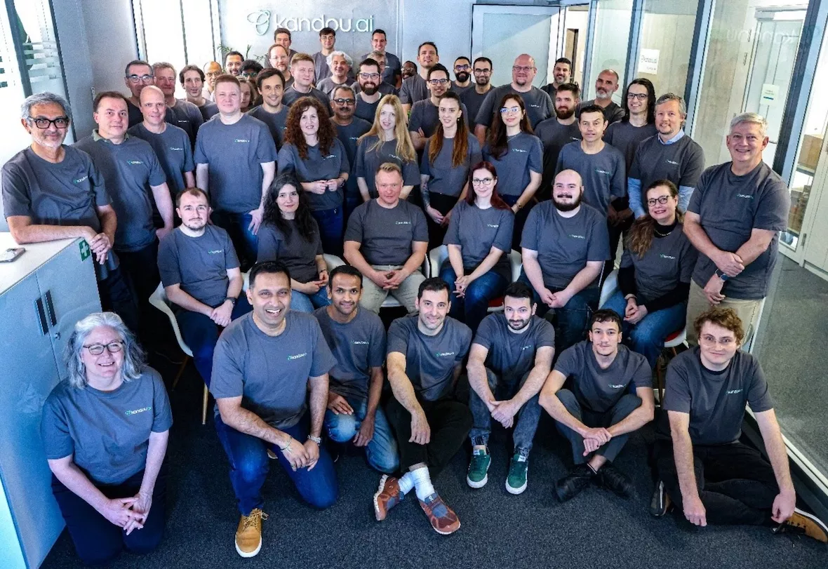 Group photo of Kandou.ai team members wearing matching gray Kandou.ai t-shirts in an office setting.