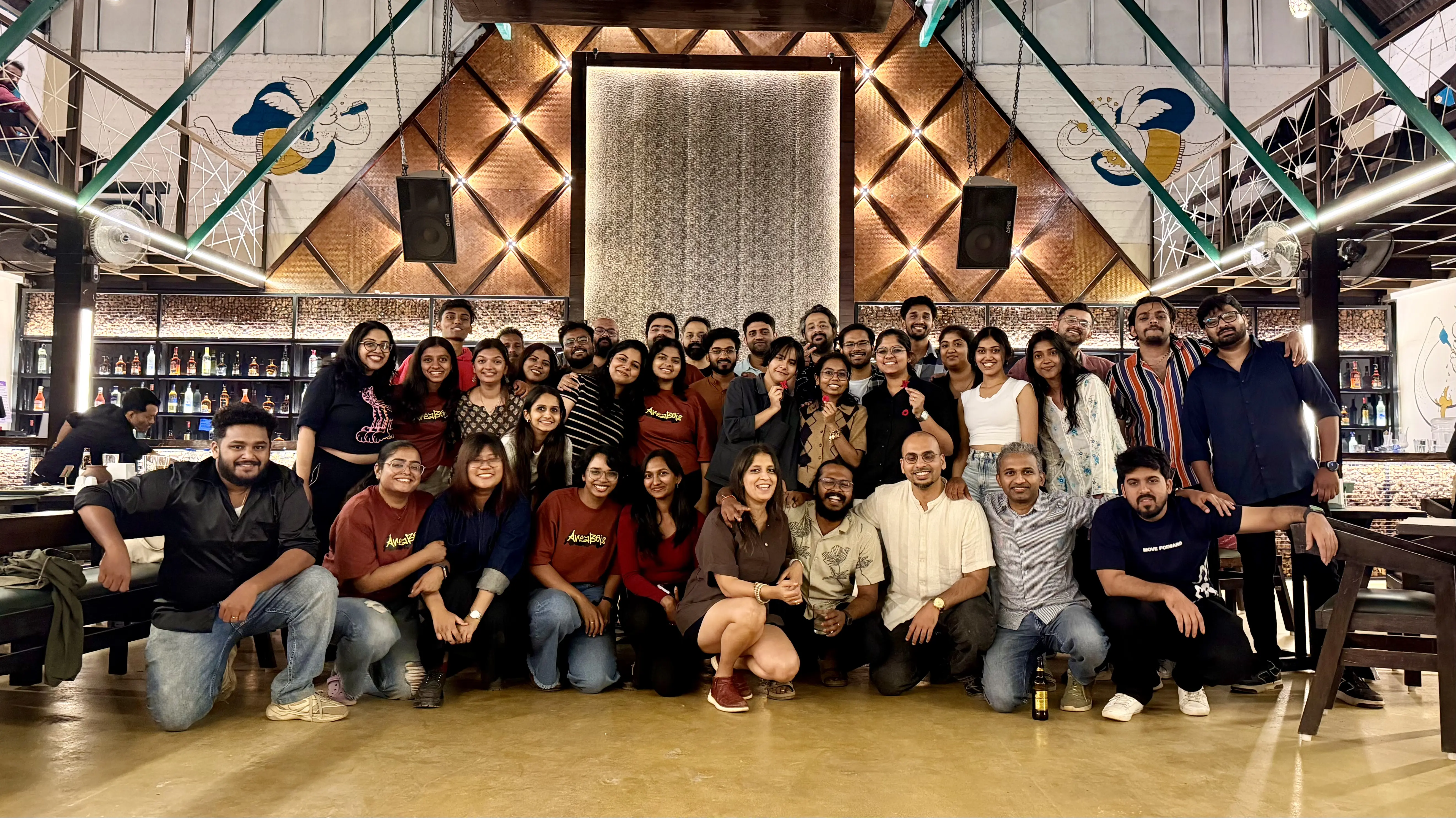 Group photo of 33 smiling adults posing in a warmly lit restaurant with a bar in the background.