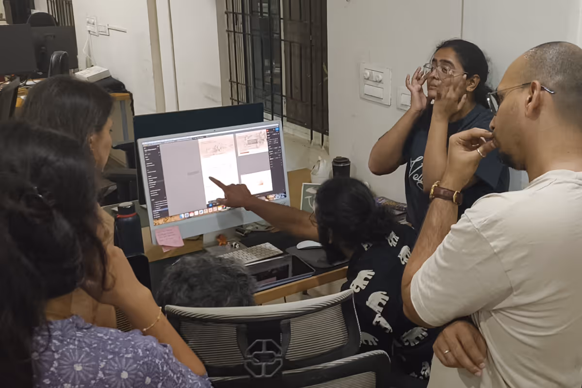Five people gathered around a desk, closely examining content displayed on a desktop computer screen in an office setting.