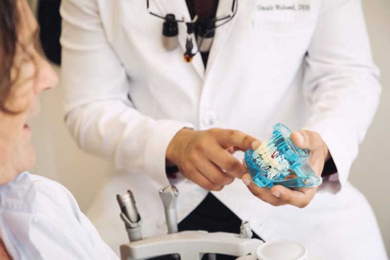 Dentist holding blue Invisalign aligner in hands during patient consultation