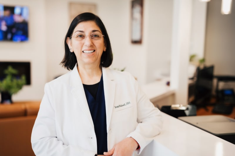 Female dentist in white coat standing in modern dental office with confident expression