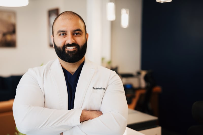 Male dentist in white coat with arms crossed in professional portrait in modern office